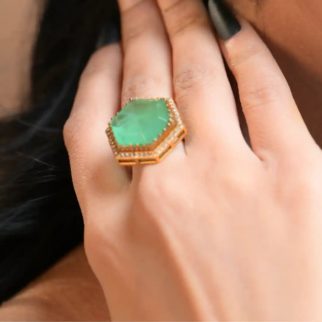 Hexagonal green gemstone ring with diamond accents on gold band, worn on finger