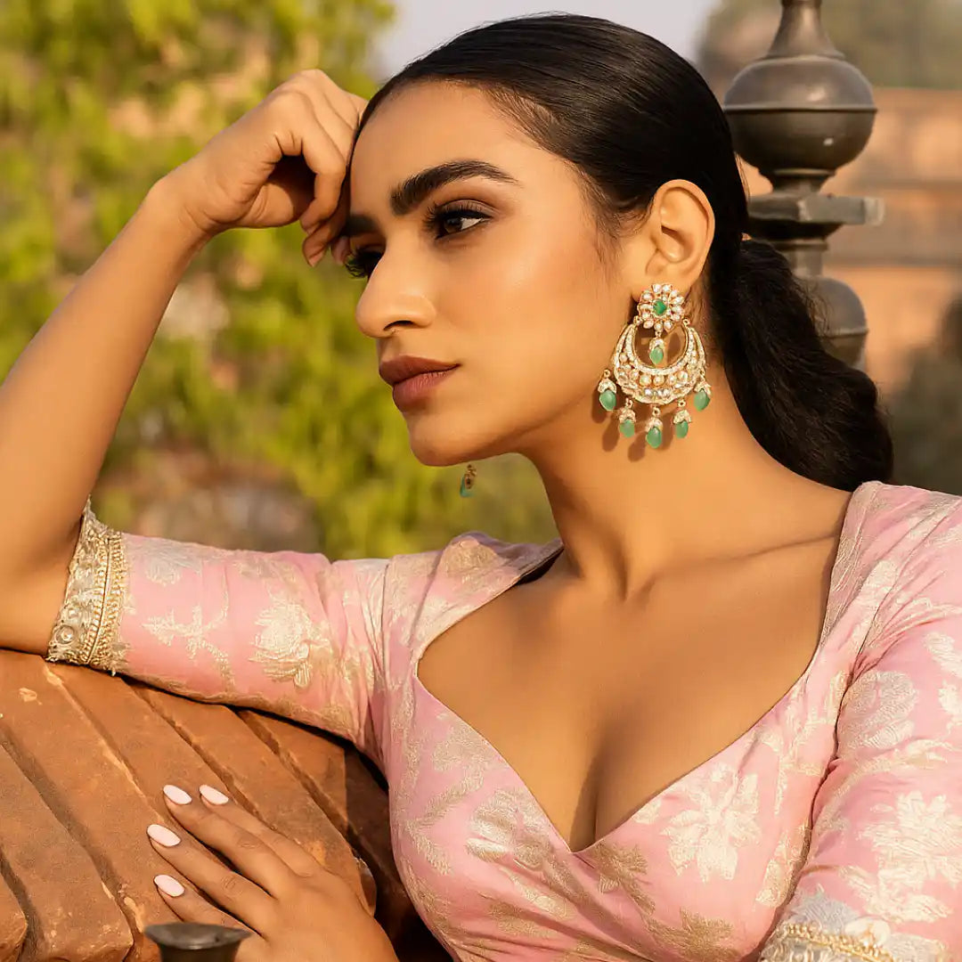Elegant woman wearing ornate silver earrings with green gemstones, styled in traditional pink attire.