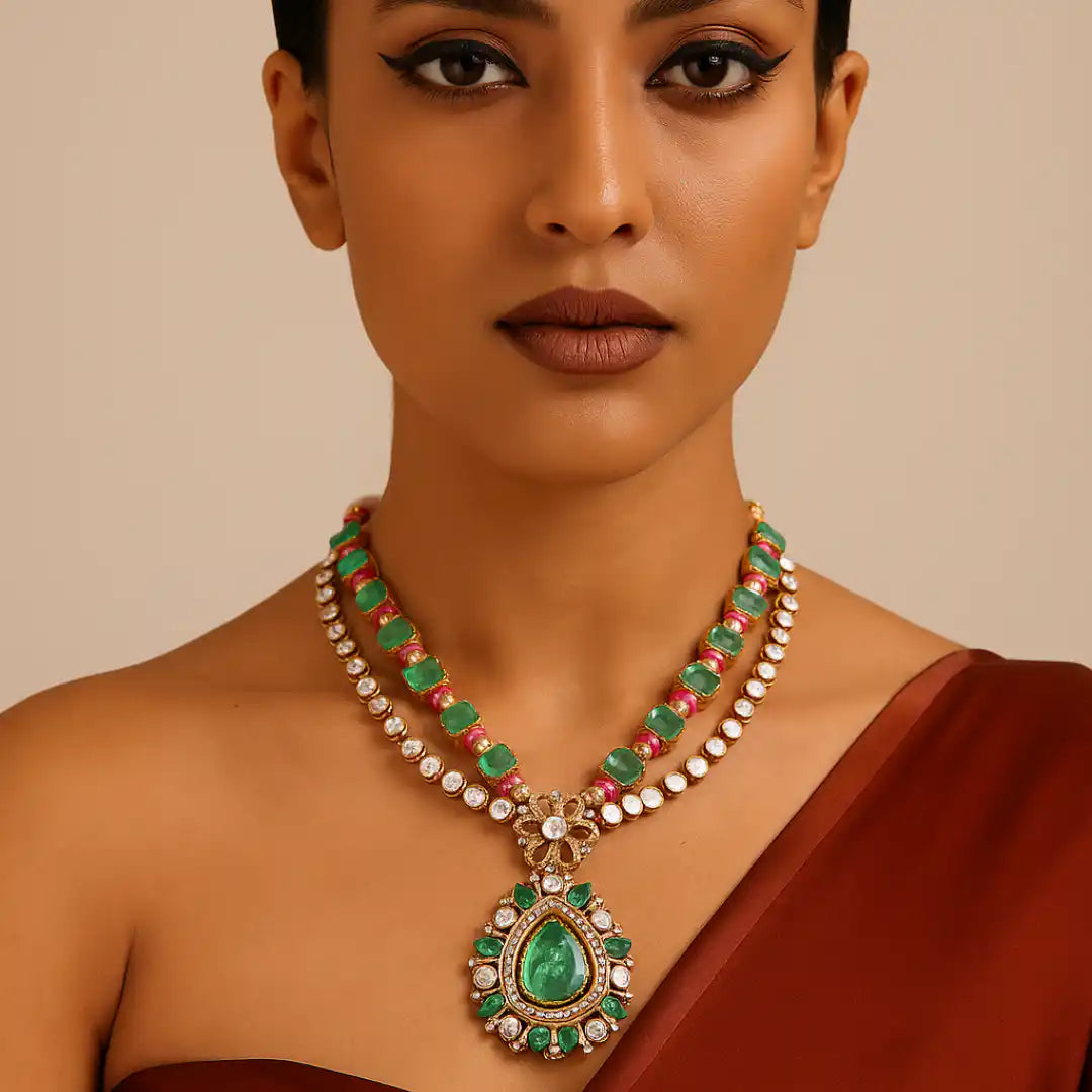 Elegant emerald and diamond necklace with intricate gold detailing, worn by woman in maroon saree