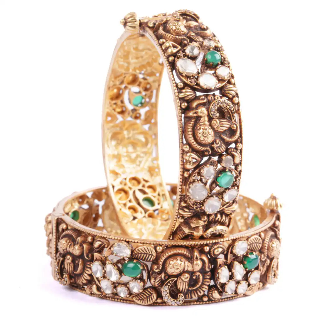 Intricate gold bangle with peacock motifs, green and white gemstones, ornate filigree design