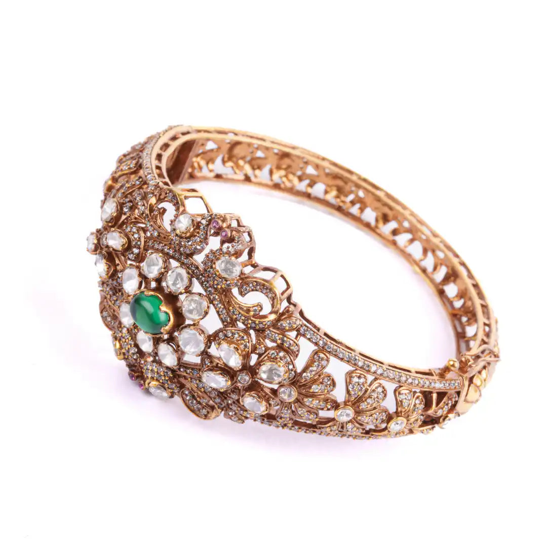 Elegant gold bangle with intricate filigree, emerald, and diamond accents, perfect for traditional or festive wear.