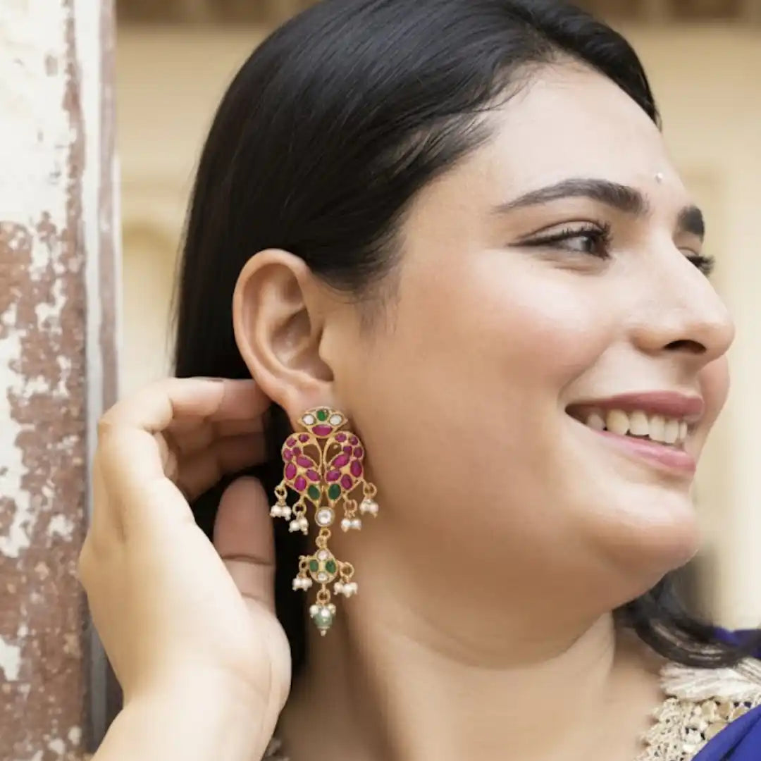 Woman wearing ornate gold earrings with pink and green gemstones, smiling softly