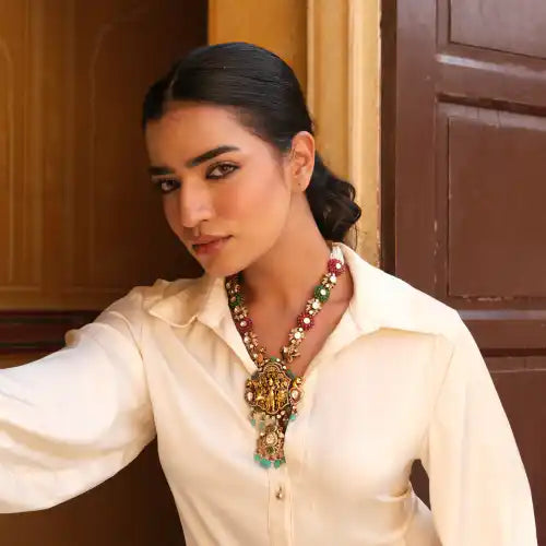 Woman wearing ornate silver necklace with colorful gemstones, styled with white blouse against wooden backdrop