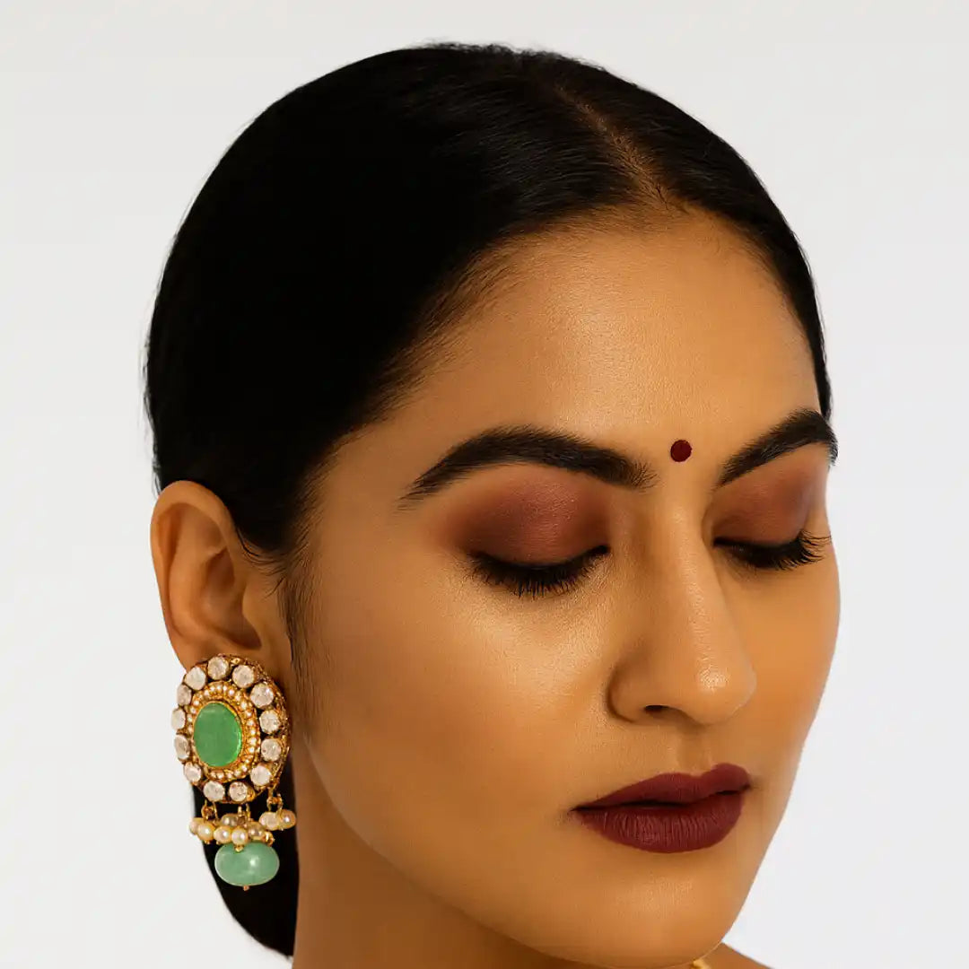 Elegant green stone jhumka earring with pearl accents, worn by woman with closed eyes