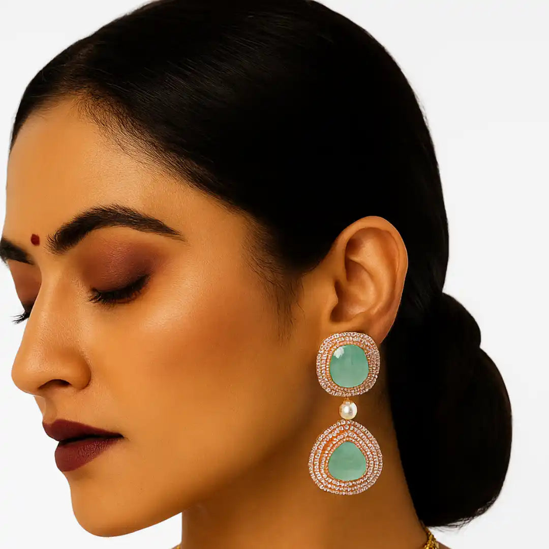 Elegant green stone earrings with diamond halo and pearl drop, worn by woman with dark hair