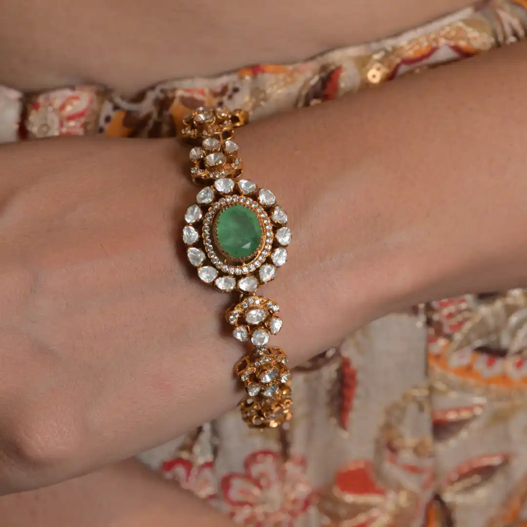 Elegant gold bracelet with emerald center and diamond accents, worn on wrist
