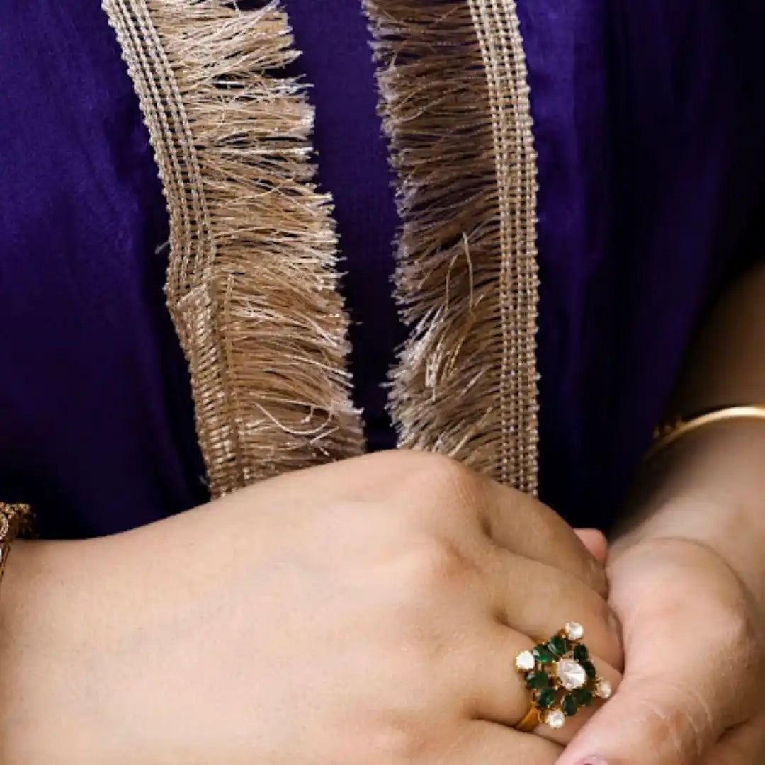 Elegant gold ring with green and white gemstones, worn with purple embroidered attire