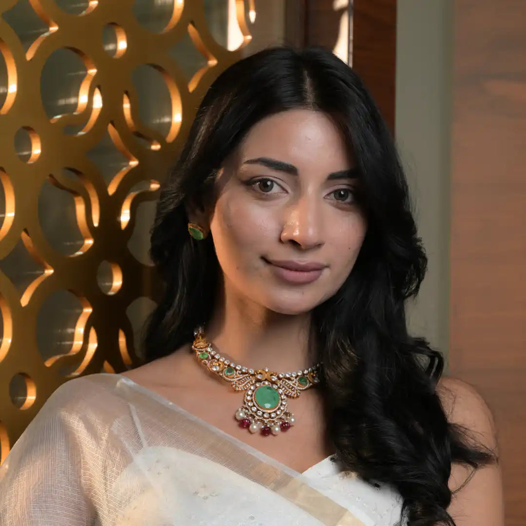 Woman wearing ornate gold necklace with green gemstone and matching earrings, elegant traditional jewelry