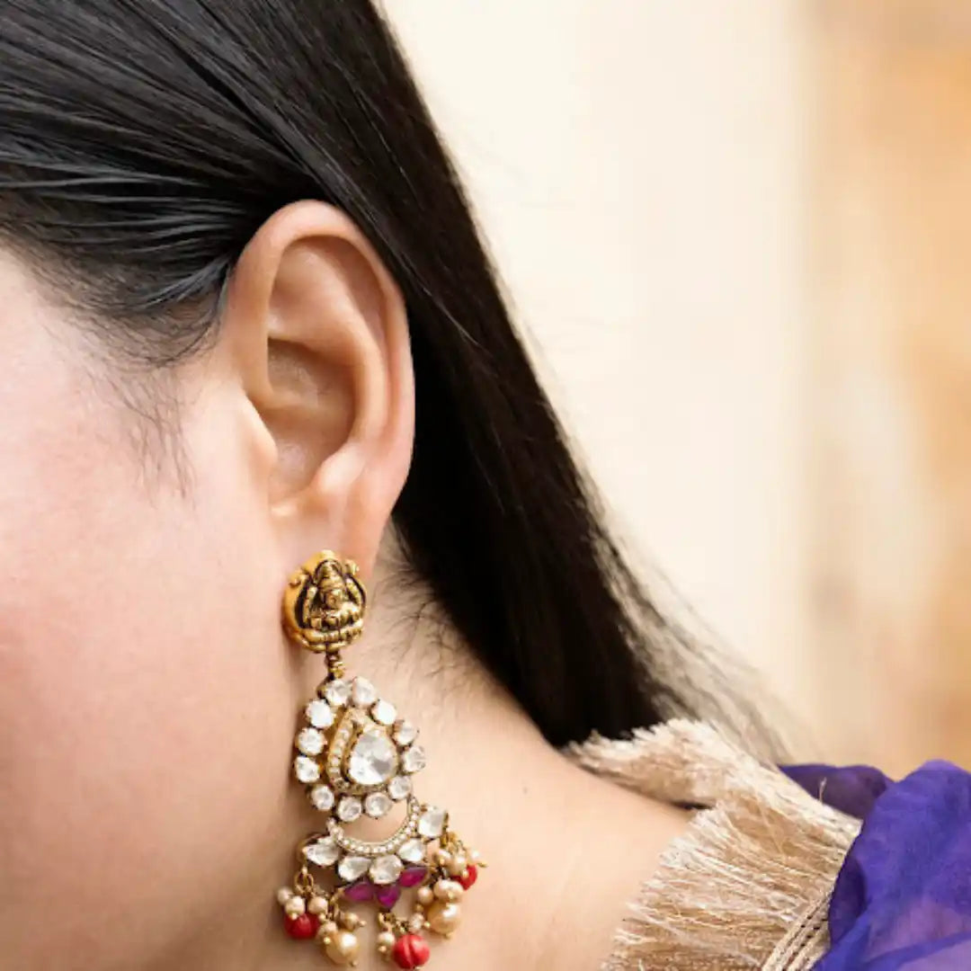 Elegant gold earring with Ganesha motif, kundan stones, and pearl drops, worn by woman in traditional attire