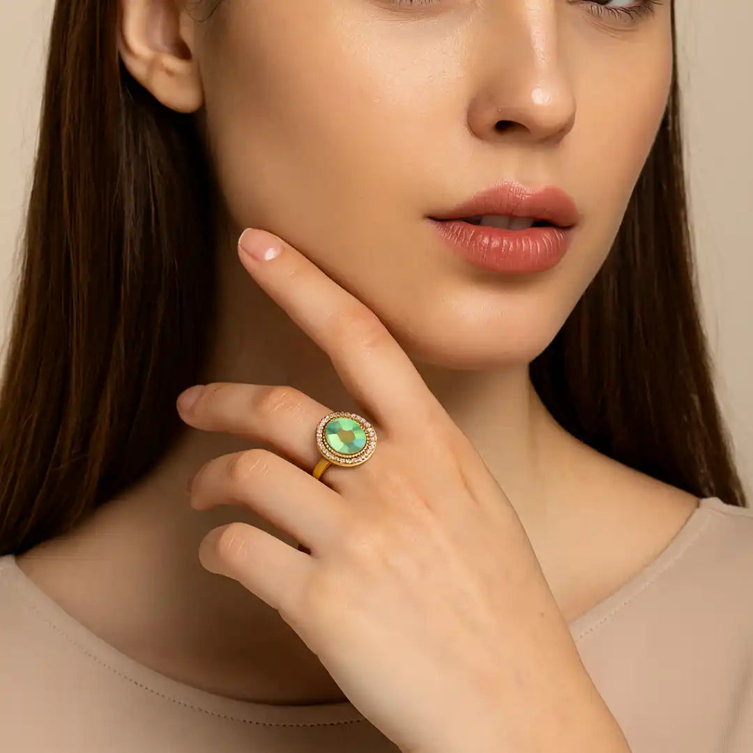 Elegant gold ring with green gemstone and diamond halo, worn by woman touching her chin