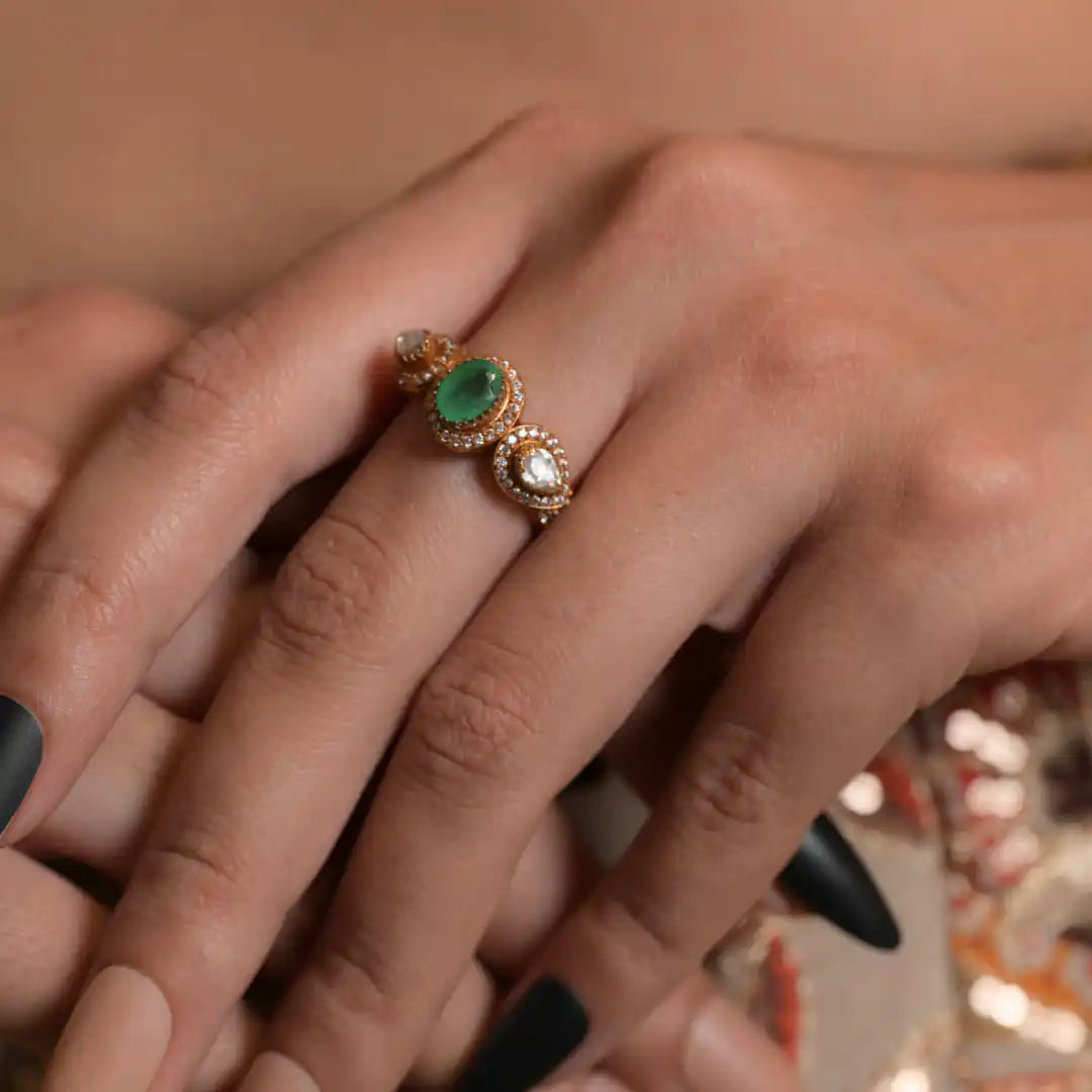 Elegant gold ring with emerald and diamond accents, worn on hand with black nail polish