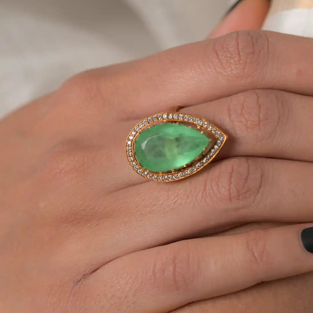 Elegant emerald ring with diamond halo on finger, gold-toned setting, luxury jewelry