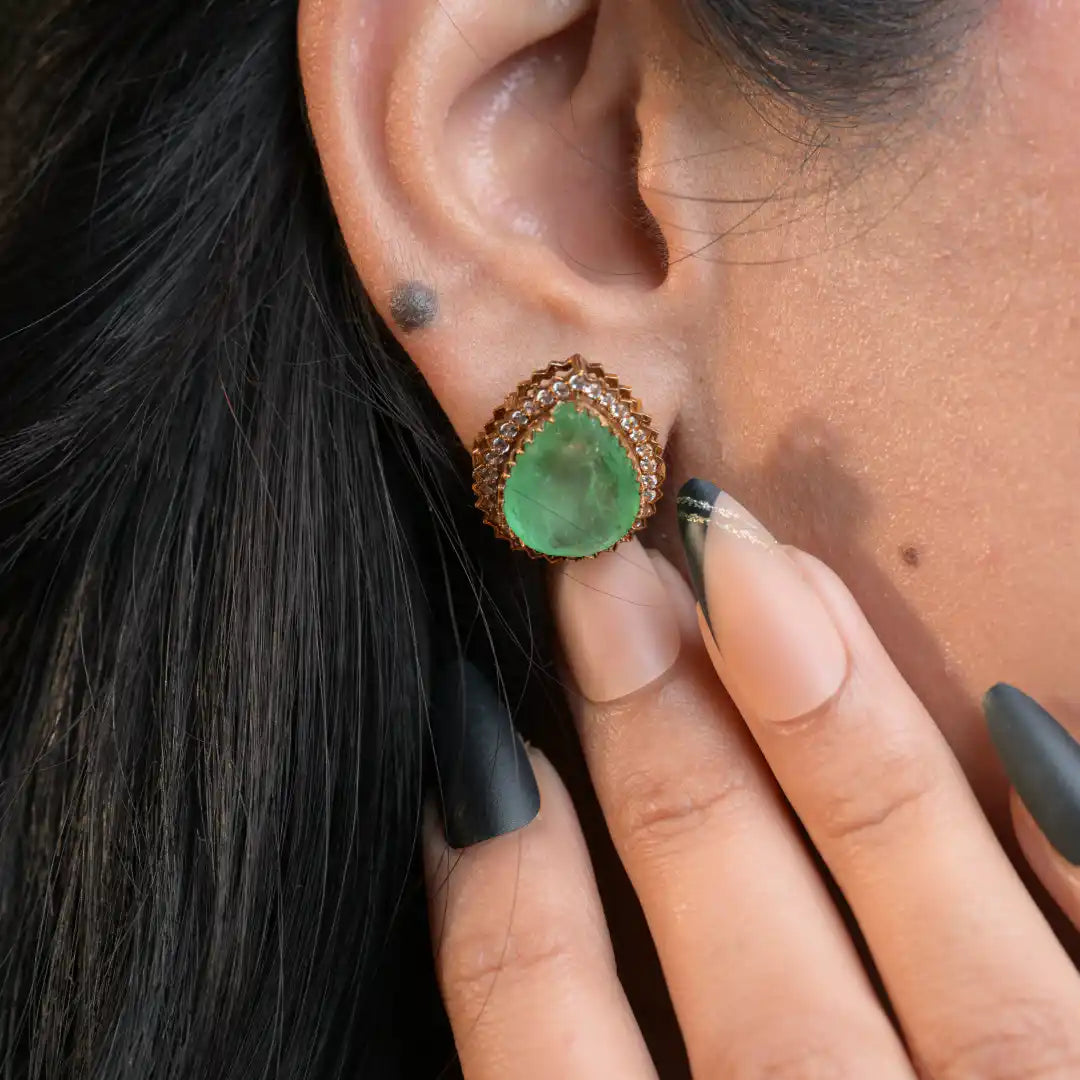 Emerald teardrop earring with diamond halo, worn on ear, elegant silver jewelry design