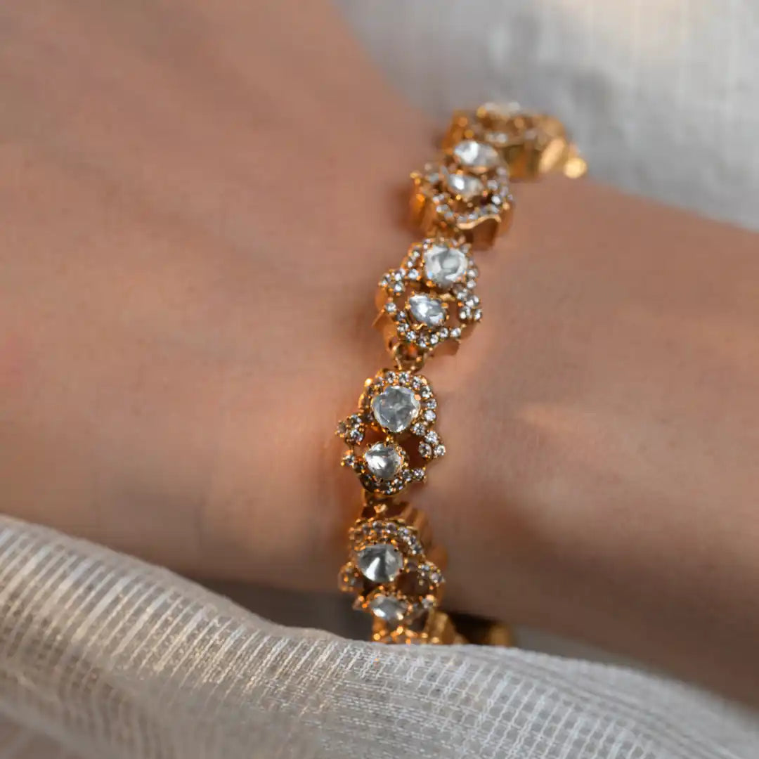Elegant gold bracelet with sparkling clear stones, worn on wrist with white fabric background