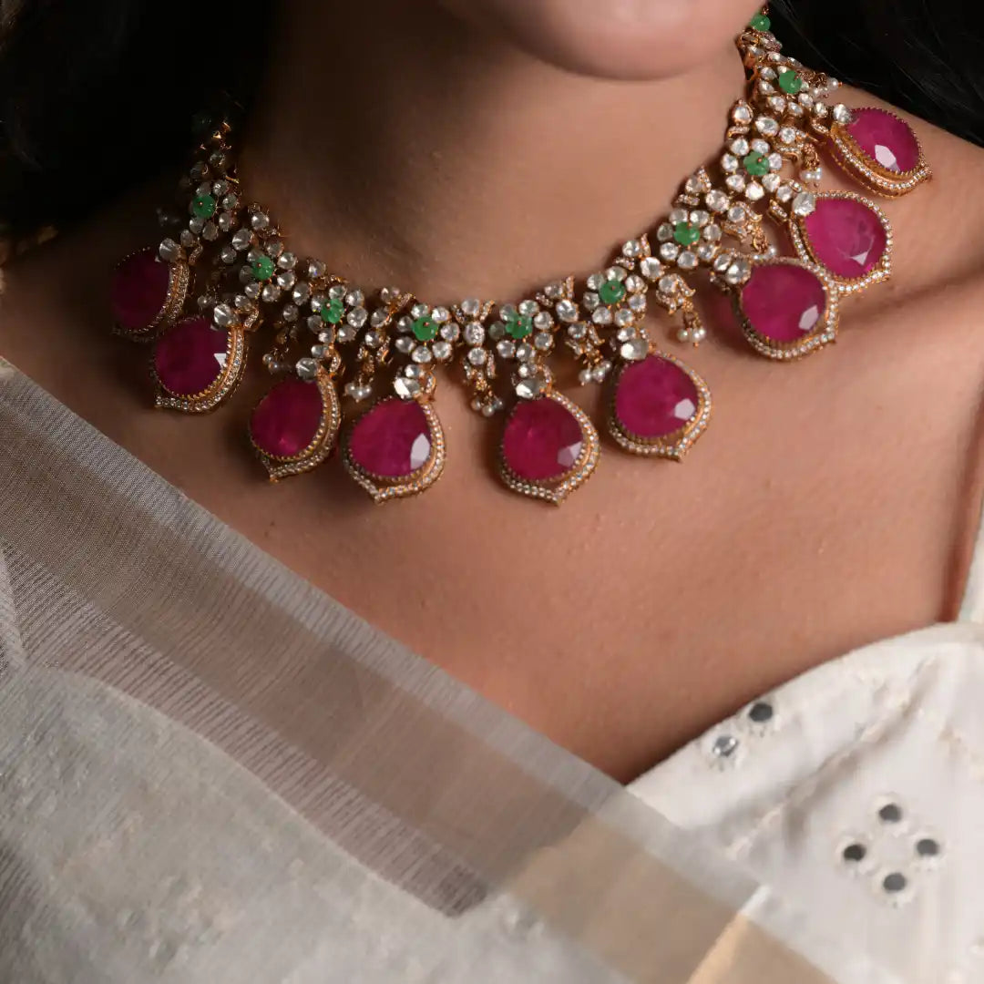 Elegant ruby and emerald necklace with diamond accents, worn with white saree for festive occasions