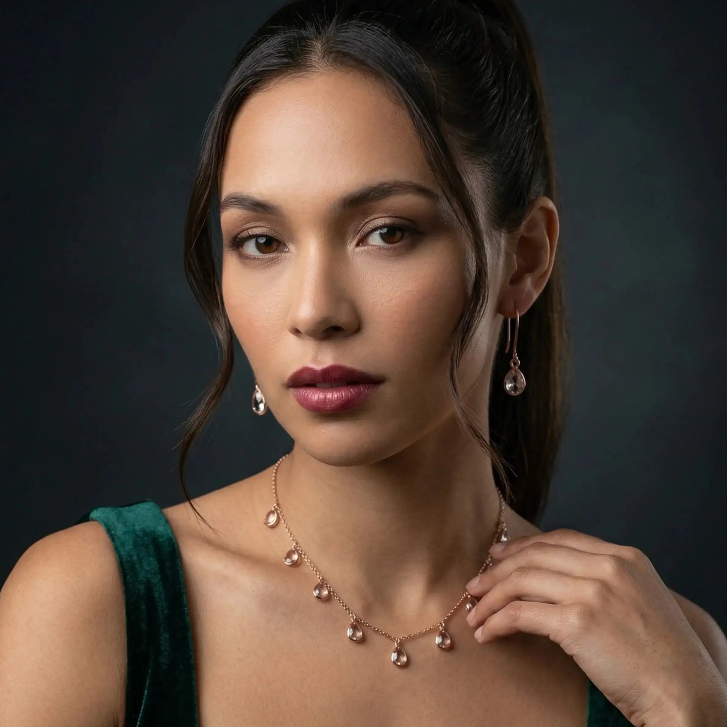 Elegant rose gold necklace and drop earrings with teardrop gemstones, styled with emerald green velvet top.