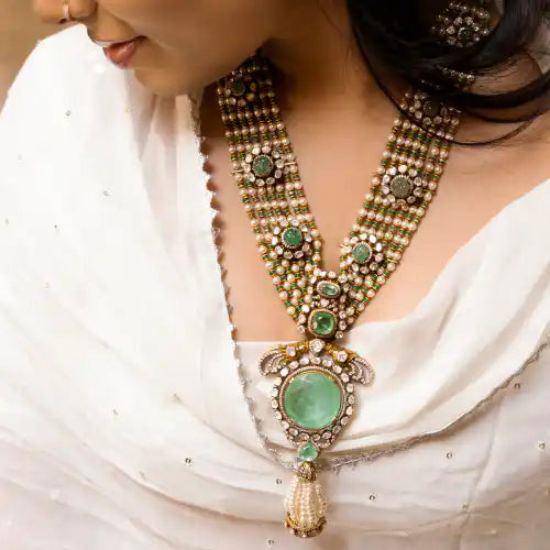 Elegant silver necklace with green gemstones and intricate beadwork, worn with white attire