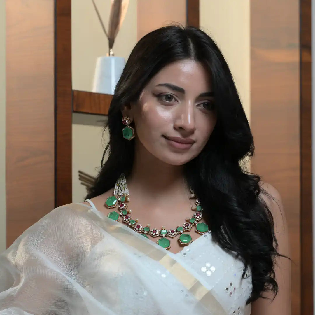 Elegant woman wearing green gemstone necklace and matching earrings, styled with white saree for festive occasions