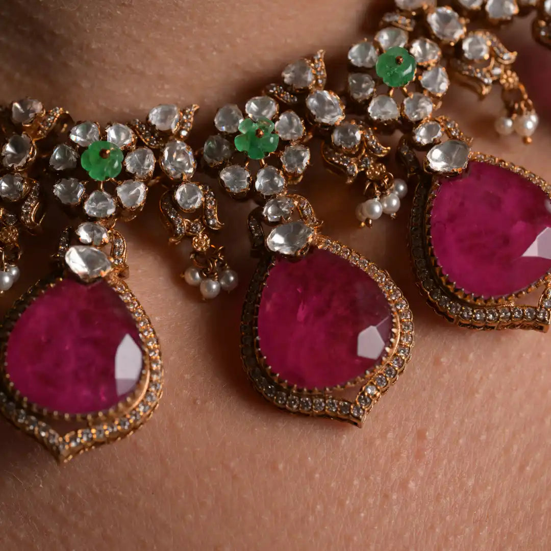Elegant gold necklace with pink gemstones, emerald accents, and pearl drops, showcasing intricate craftsmanship.