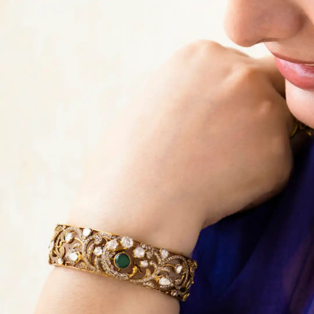 Elegant gold bangle with green gemstone and diamond accents, worn on wrist