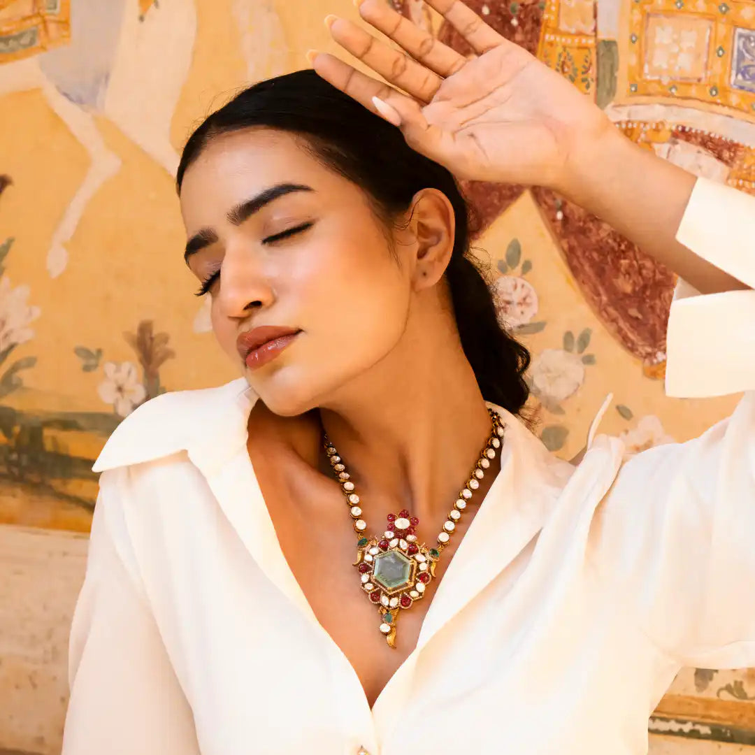 Woman wearing ornate silver necklace with gemstones and pearls, styled against vintage floral backdrop