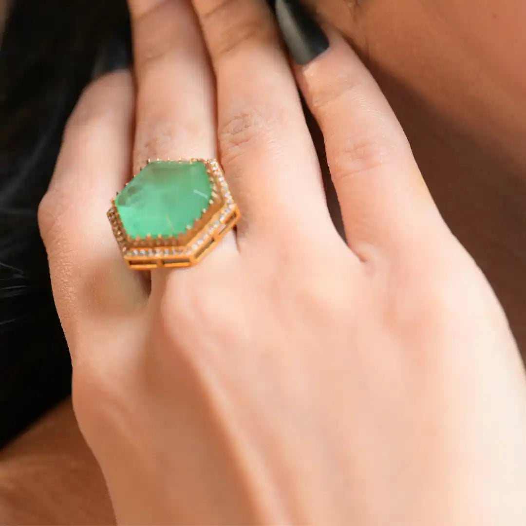 Hexagonal green gemstone ring with diamond accents on gold band, worn on finger