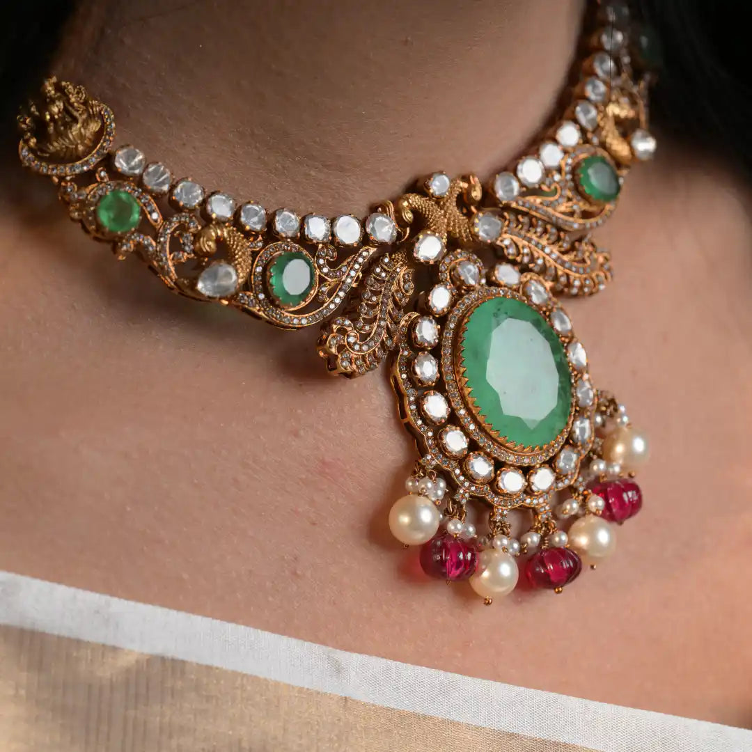 Elegant gold necklace with emerald, ruby, and pearl accents, showcasing intricate craftsmanship.