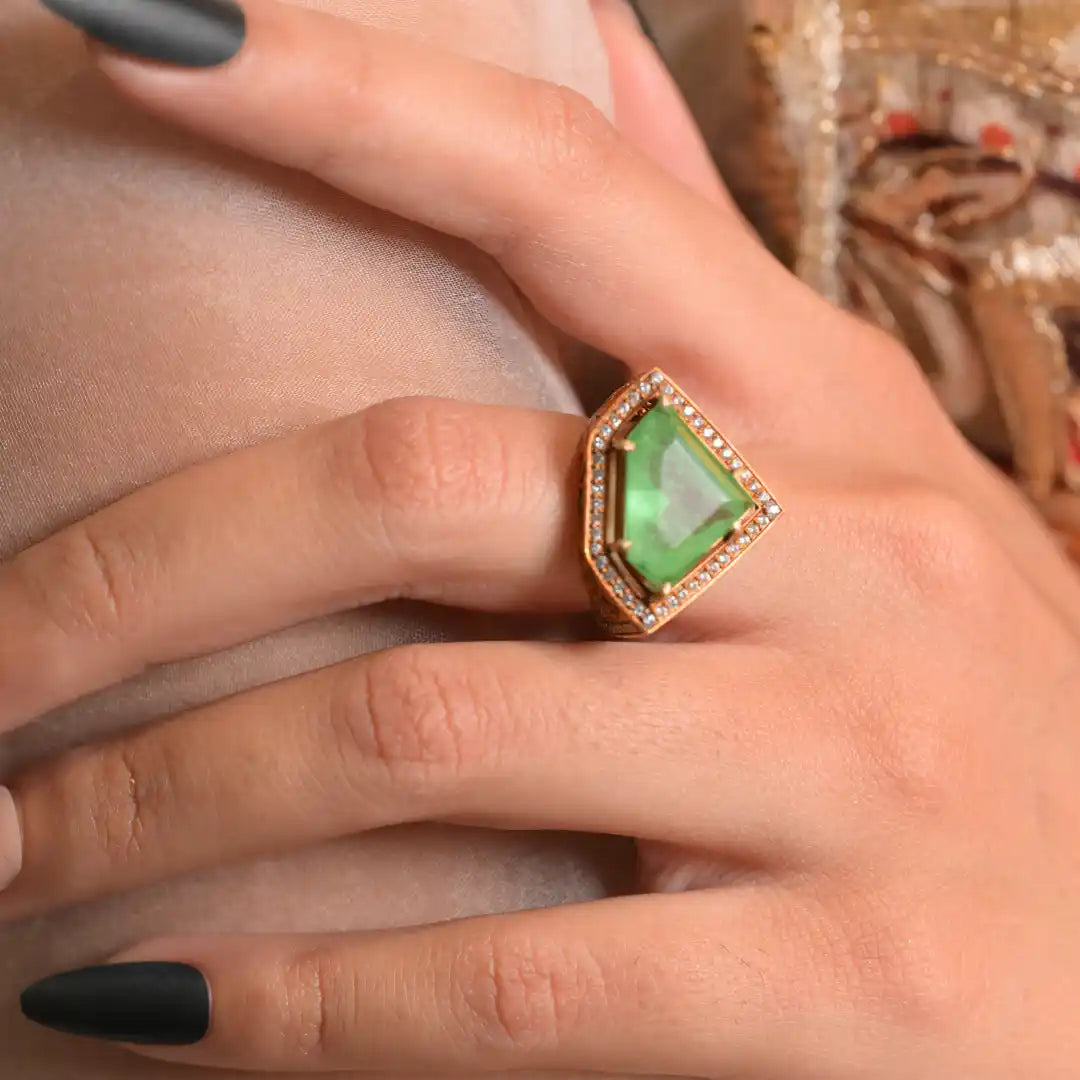 Emerald green gemstone ring with diamond halo on woman's hand, elegant silver jewelry