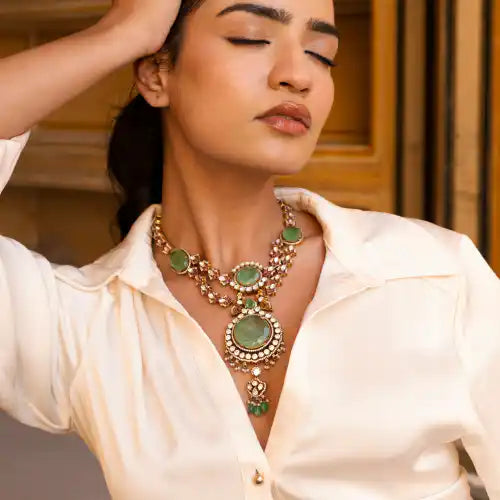 Elegant woman wearing ornate green gemstone necklace with intricate silver detailing, exuding timeless luxury.