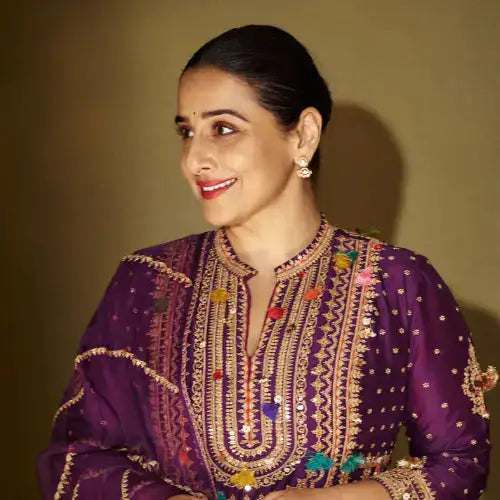 Woman in purple embroidered kurta with gold detailing and colorful embellishments, wearing silver earrings