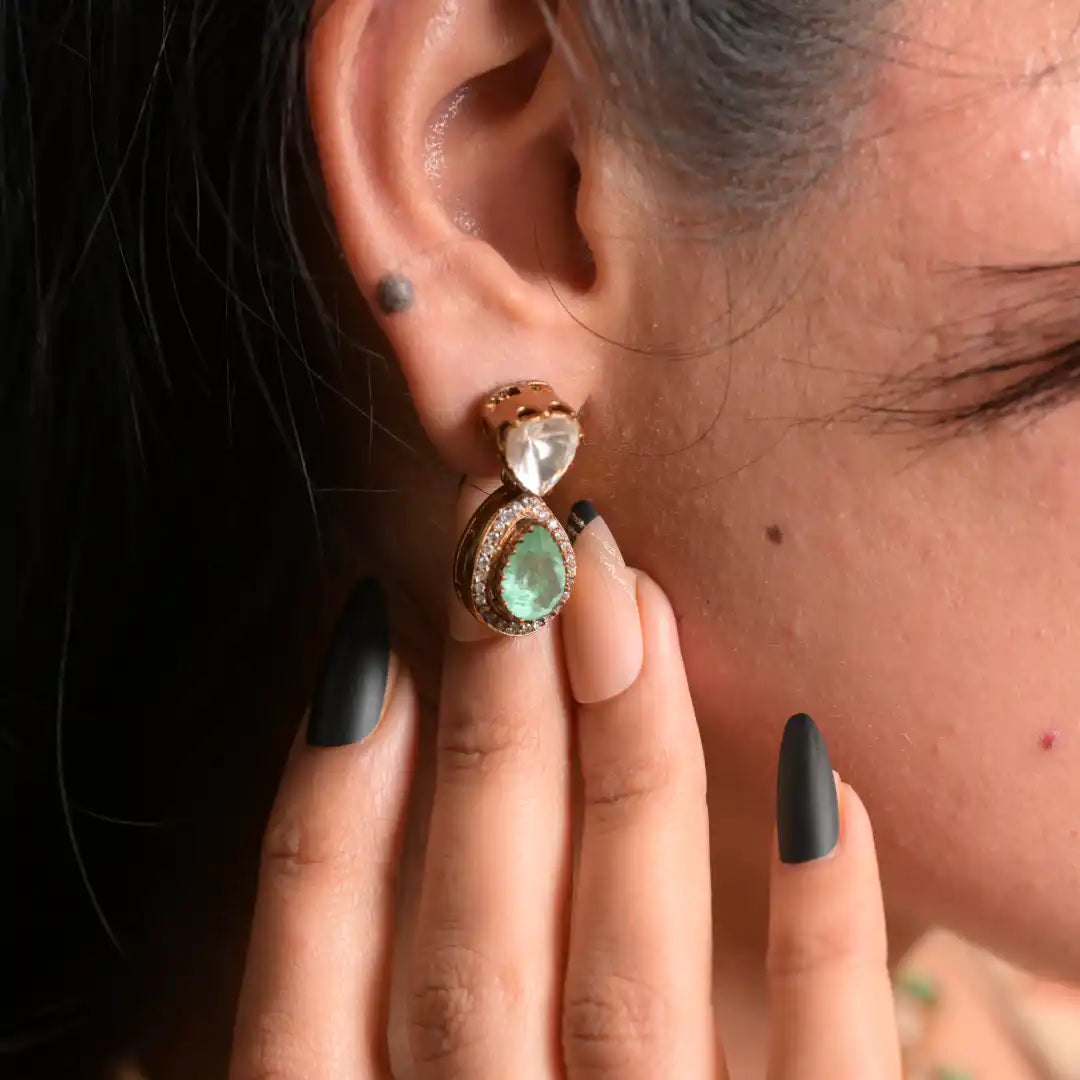 Elegant silver earring with green gemstone and diamond accents, worn on ear with black matte nails.